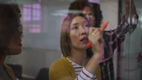 diverse work colleagues writing and drawing on glass wall having a discussion