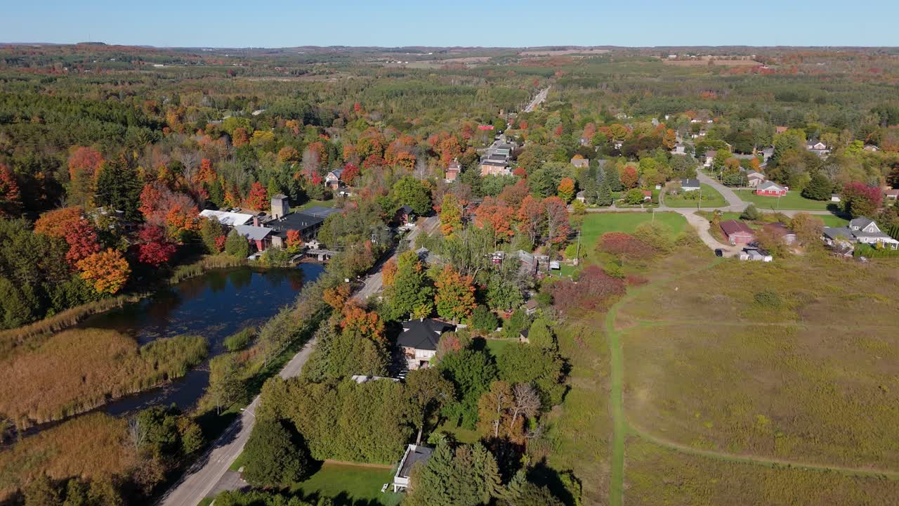 A beautiful, wide aerial shot of the village of Alton, Ontario, and its surrounding rural landscape, showcasing the stunning colours of the autumn season from a high altitude