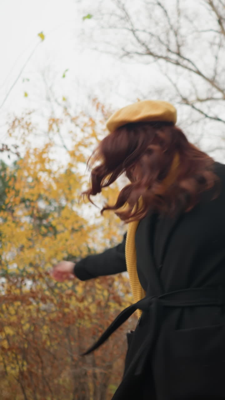 mujer alegre con boina amarilla y gafas de sol juguetón gira alrededor, su silenciador amarillo balanceándose en la brisa, mientras disfruta de un vibrante día de otoño en el bosque