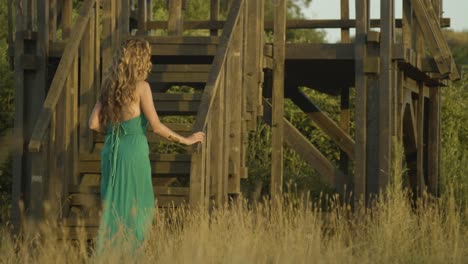 gorgeous caucasian model in green dress walks up to wooden stairs at golden hour