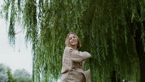 mujer feliz en un abrigo beige bajo un sauce