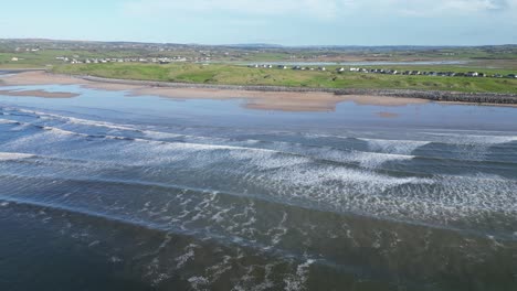 aerial descending shot of waves crashing at lahinch beach with seafront houses