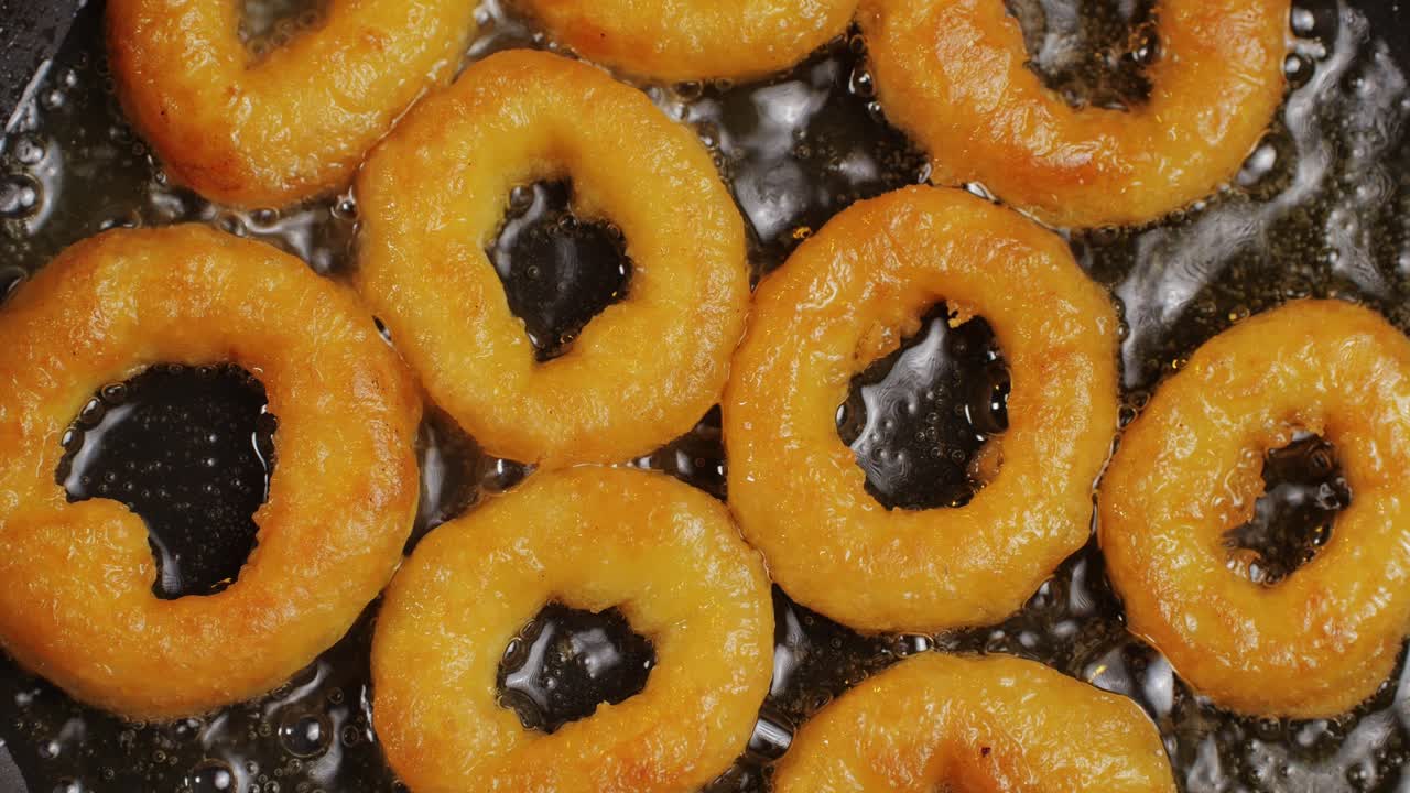 Fried crispy onion rings in a frying pan with boiling oil top view. Roasted onion rings for snacks at bar, cafe. Fast food. Delivery. Beer snacks