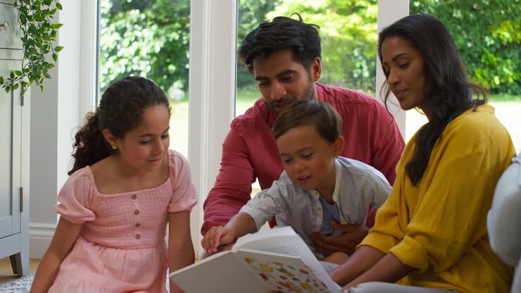Smiling Family At Home Sitting On Floor In Lounge Reading Book Together