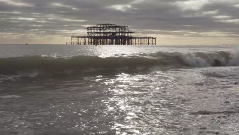 small wave braking in brighton city beach, england uk. famous burnt pier in the distance