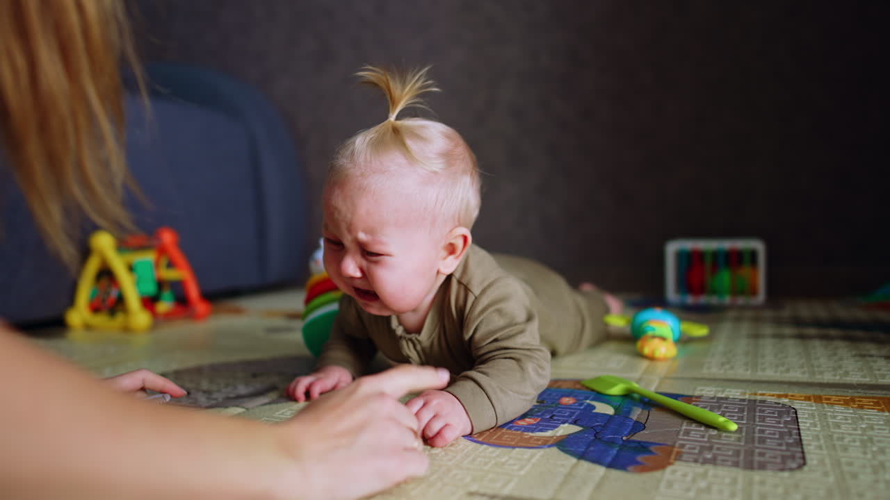 Infant baby boy lying on the floor crying bitterly. Mother approaches to calm down her son but he doesn't stop. Close up.