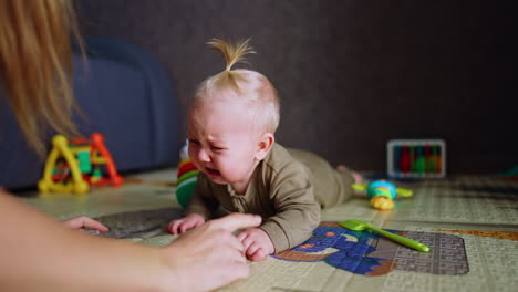 infant baby boy lying on the floor crying bitterly. mother approaches to calm down her son but he doesn't stop. close up.