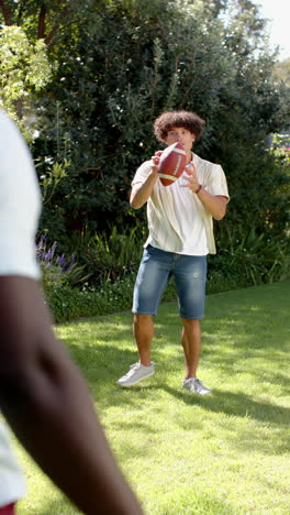 vertical video: friends playing catch with football in sunny backyard, enjoying outdoor fun