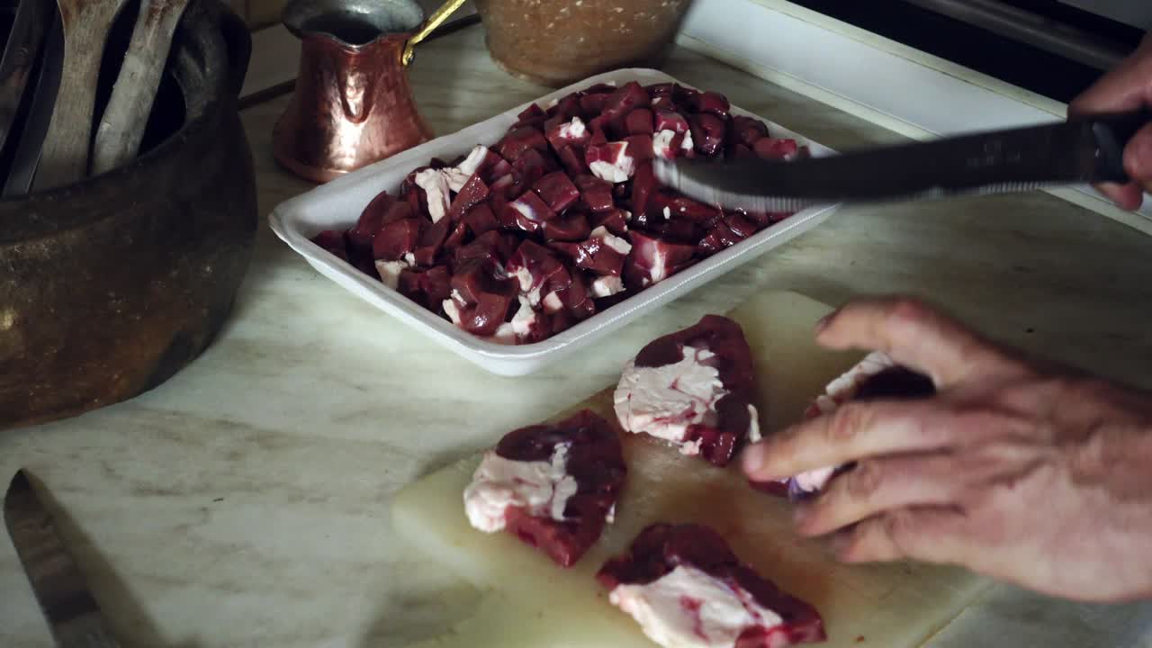 Senior Turkish male chopping liver meat on chopping board at his kitchen to serve in iftar in Ramadan Month with historical kitchen tools on background