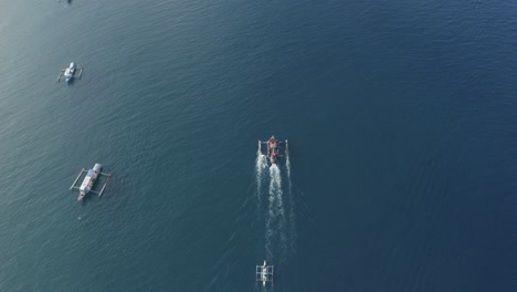 top view footage of a small and big running fishing boats on a crystal clear turquoise blue water on a tropical island in the philippines - aerial drone