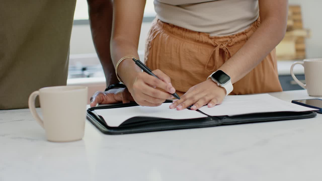 Indian woman reviewing pages, opening folder, signing forms with pen while partner watching at home