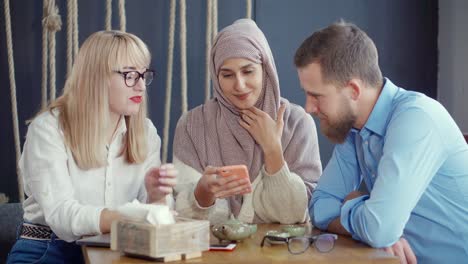 three people looking at a smartphone in a cafe