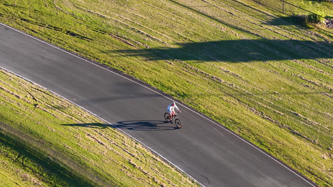 A teenager rides a bicycle along a sunlit path in Gold Coast, Australia, casting long shadows on the grass
