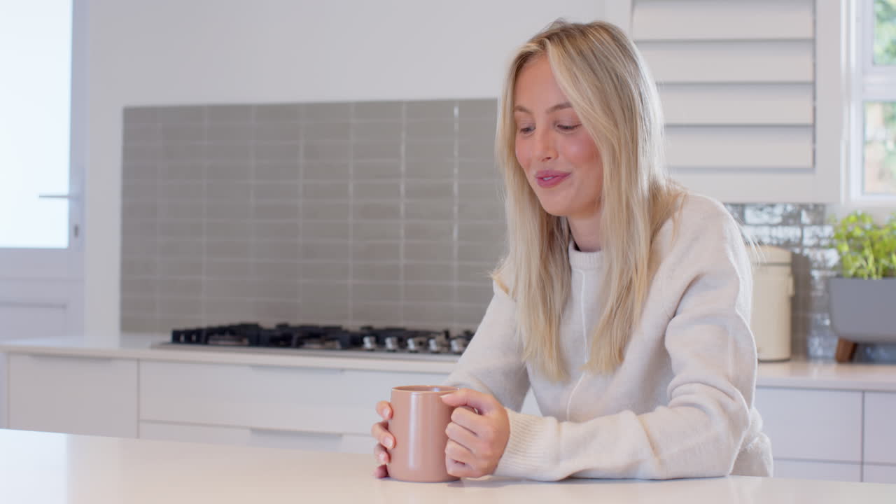 Smiling woman enjoying coffee at home, relaxing in cozy kitchen, copy space