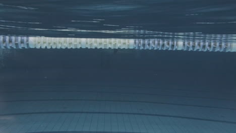 foto lateral submarina de una joven nadadora con gorro de baño y gafas de buceo en una piscina cubierta