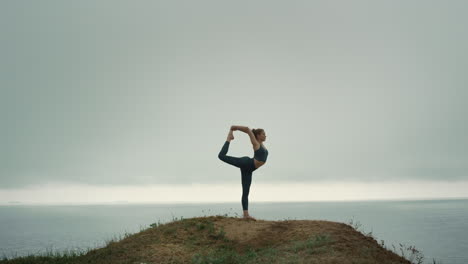 Fit-woman-standing-one-leg-stretching-on-hill.-Girl-doing-gymnastic-exercise.