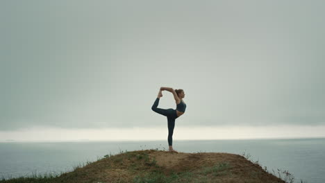 fit woman standing one leg stretching on hill. girl doing gymnastic exercise.