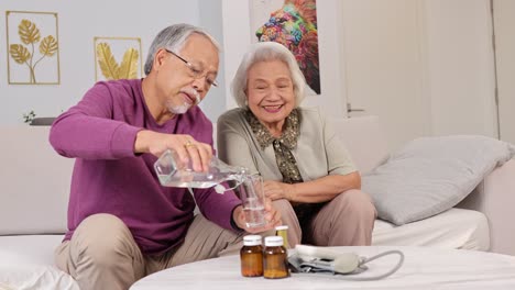 an elderly couple sits together, sharing a caring moment as one pours water for the other in a cozy living room