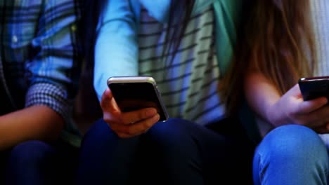 sección media de amigos de la escuela usando teléfono móvil en el pasillo