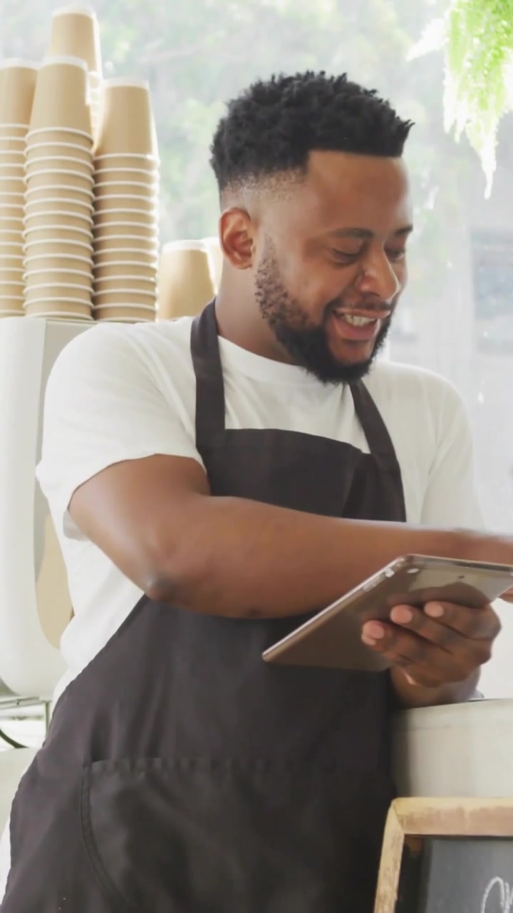 Vertikal video: Barista tapper på tablet og tjekker salgsdata ved disken, animerede diagrammer stiger.