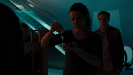 people conducting an experiment with a test tube in a dark, futuristic setting with escalators