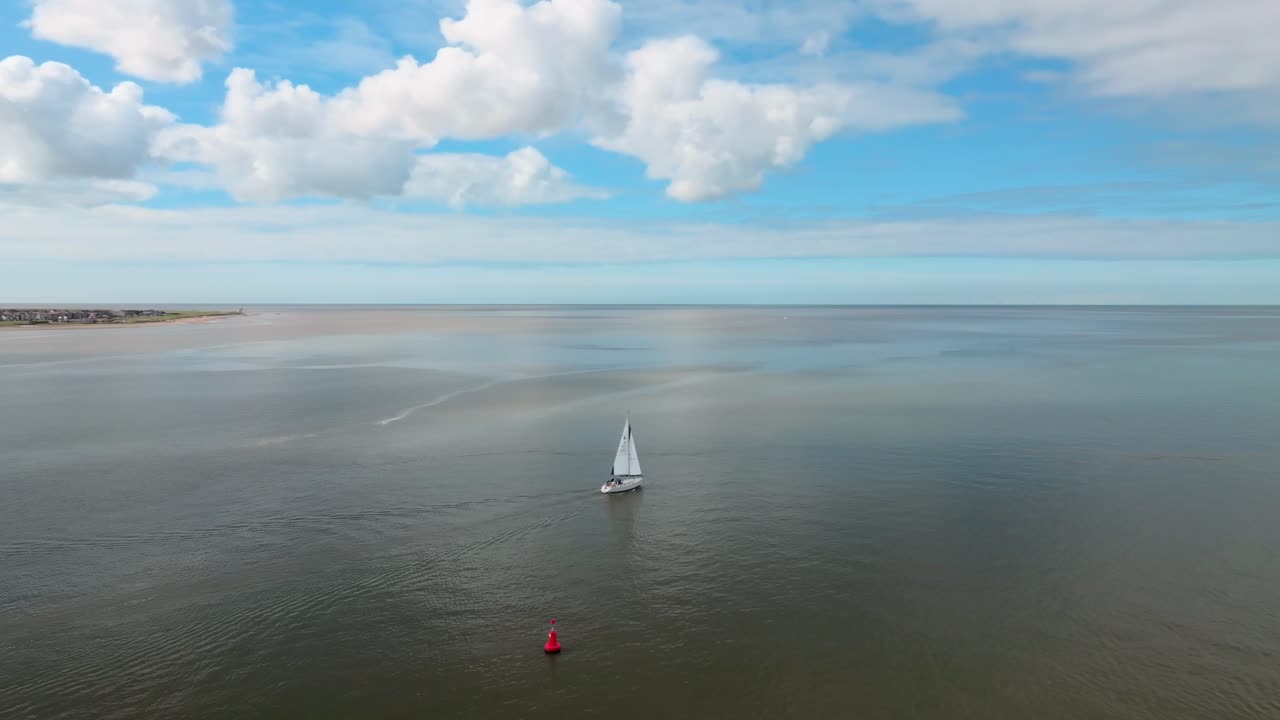 Yacht Heading Out To Sea On Calm Water With Clouds Reflecting In Dark Water. River Wyre Estuary. Slow Camera Rotation Showing Coastline. Fleetwood, Lancashire, UK