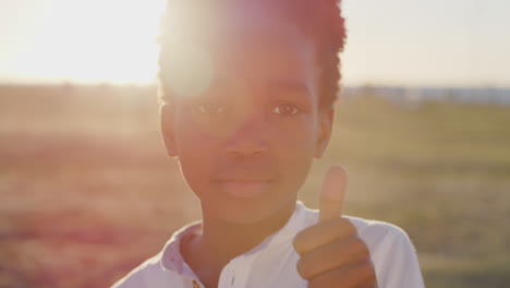retrato de cerca pequeño niño afroamericano pulgares hacia arriba sonriendo feliz disfrutando del parque costero puesta de sol fondo esperanzador juventud positiva