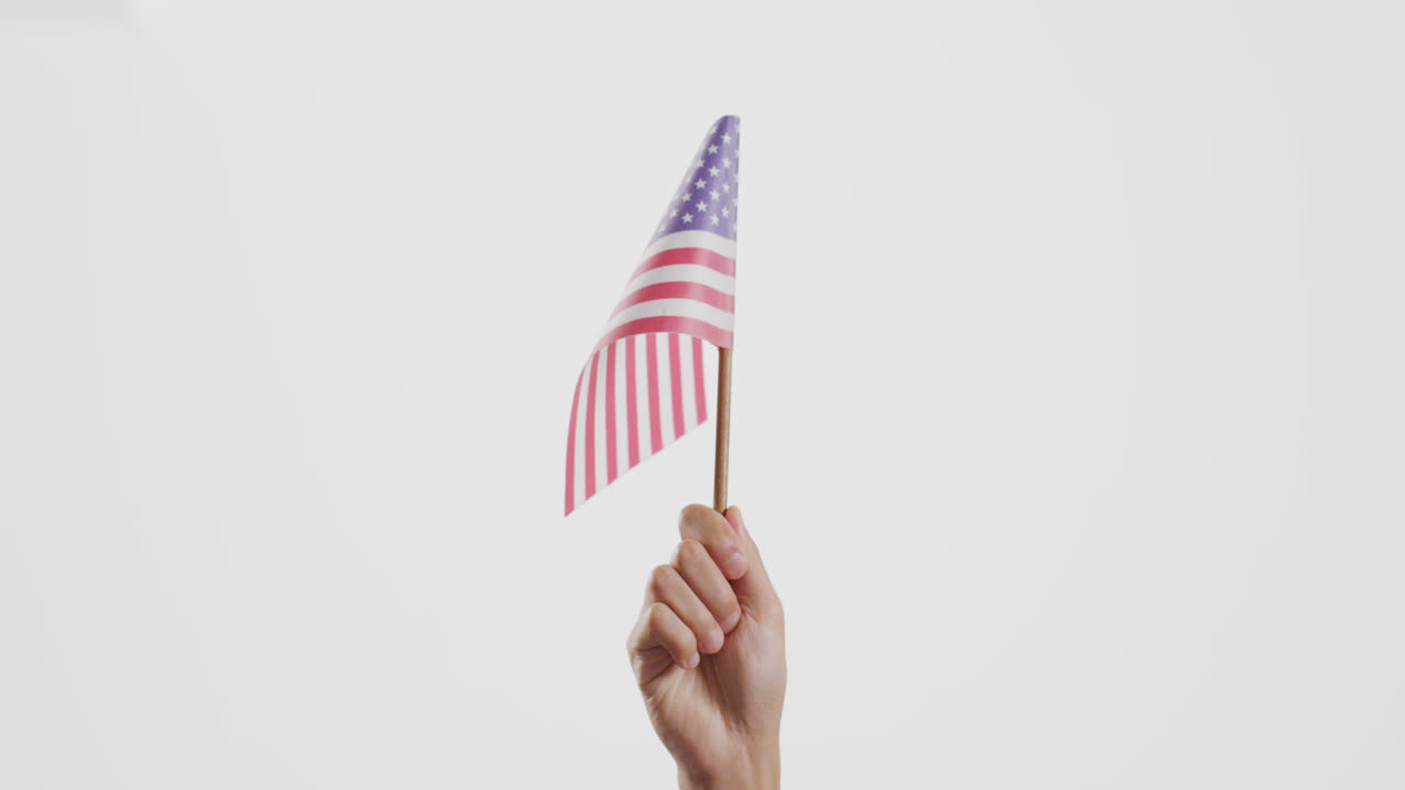 Primo piano di una mano che regge la bandiera nazionale degli USA su sfondo bianco con spazio per il testo