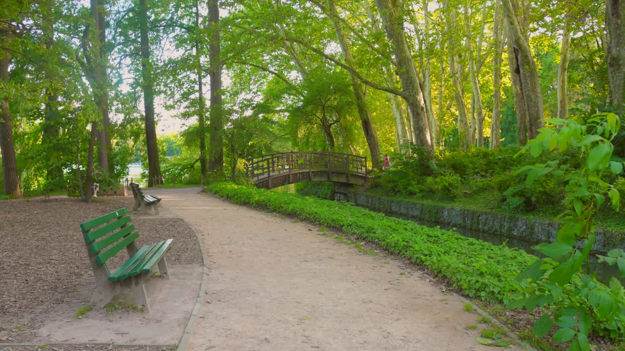 Explore the tranquility of Park of the Golden Head with its winding path, lush trees, peaceful benches, and a charming bridge over the flowing river.