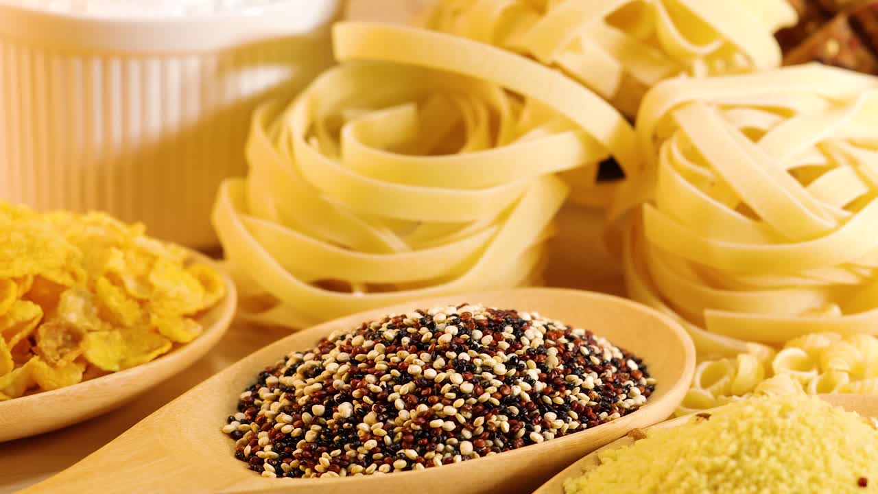 A close-up view of various grains and pasta arranged under warm lighting, highlighting textures and colors