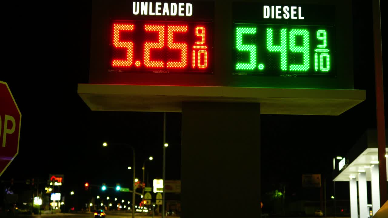 Gas station prices LED light up sign for regular and diesel fuel at night over 5 dollars per gallon credit and cash price, during 2021 2022 war time recession, ground up shot with cars driving by