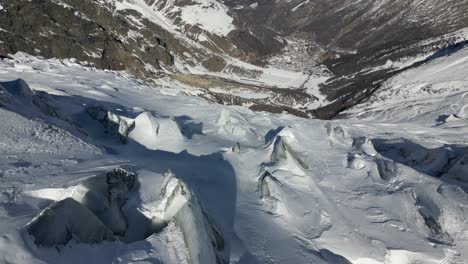 Aerial-view-of-a-mountain-steep-facade-in-the-Swiss-alps-in-winter,-valley-downhill