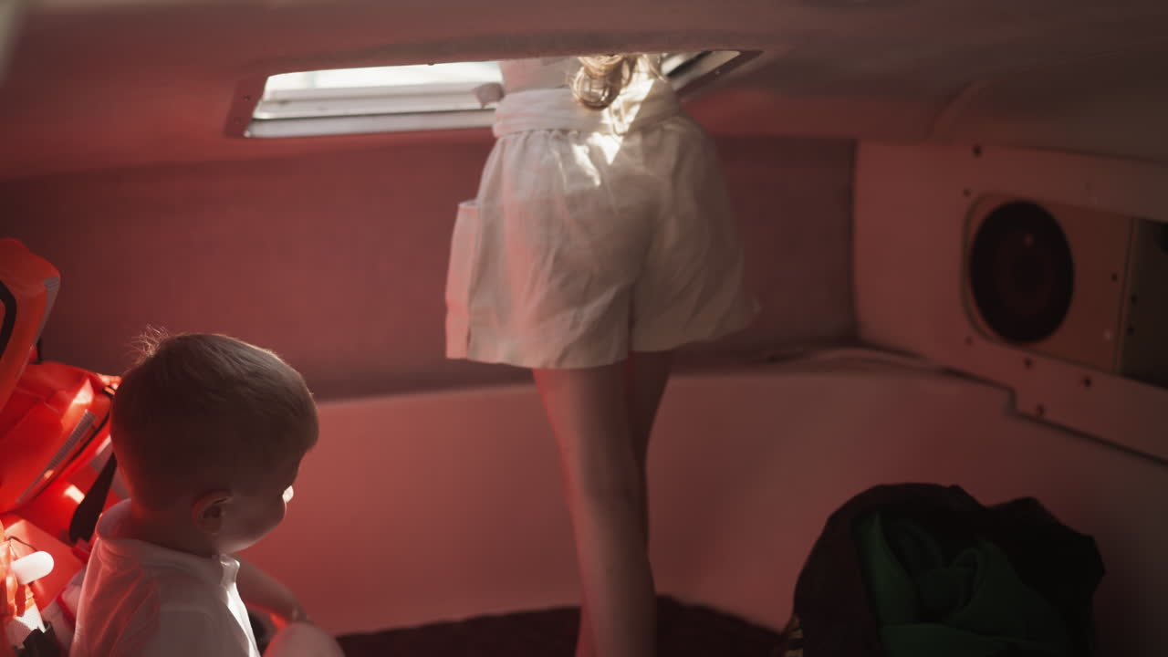 маленькая девочка смотрит из выхода из каюты, в то время как брат сидит рядом на моторной лодке. дети путешествуют на яхте в летний семейный отпуск. мальчик и девочка на лодке