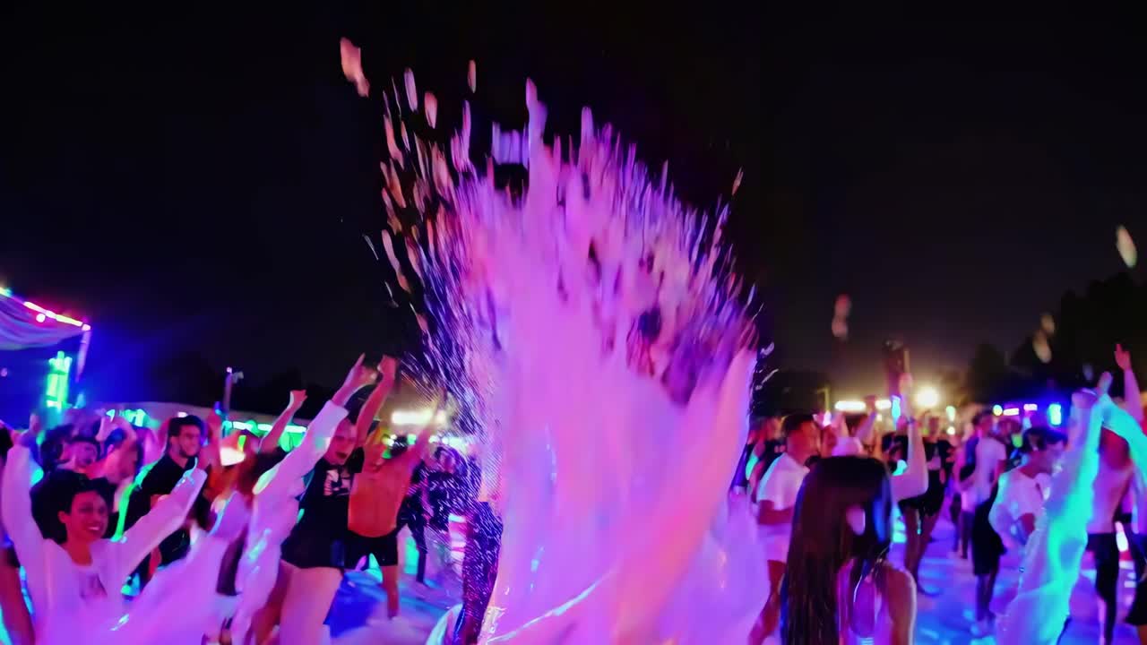 Energetic foam cascading over jubilant partygoers dancing beneath vibrant lights, generating electric atmosphere of pure celebration and collective joy during summer music festival