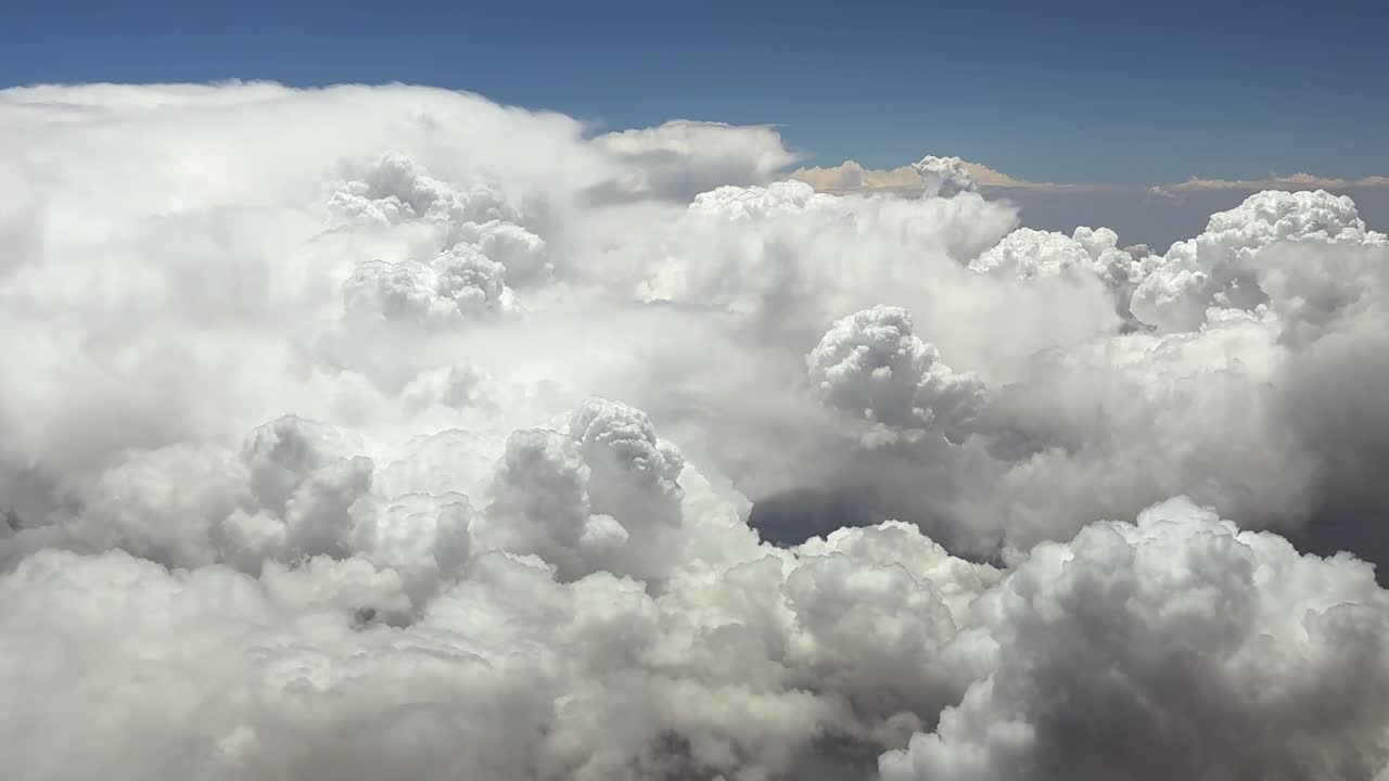 A Pilot’s perspective taken from inside the cockpit of a jet airplane flying at very high altitude at cruise over threatening storm clouds under a blue sky. Ultra-realistic aerial shot.