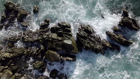 drone hovering over rocks in the ocean as waves crash