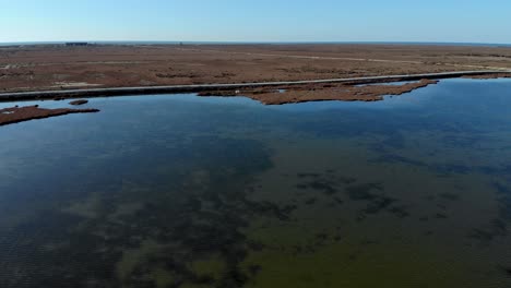 tranquil shallow lagoon with calm clear water bordered by brown grassland with reeds and marshland under clear bright sky
