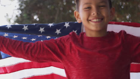 portrait of proud hispanic boy wrapped in stars and stripes american flag running towards camera