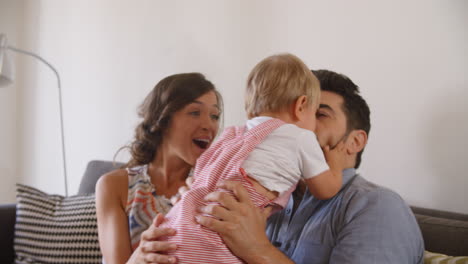 Parents-Playing-With-Baby-Son-On-Sofa-At-Home