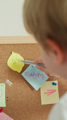 preschooler draws sun with pen on leaf of colored paper slow motion. boy learns to draw playing with cork board backside view. child develops artistic skills closeup