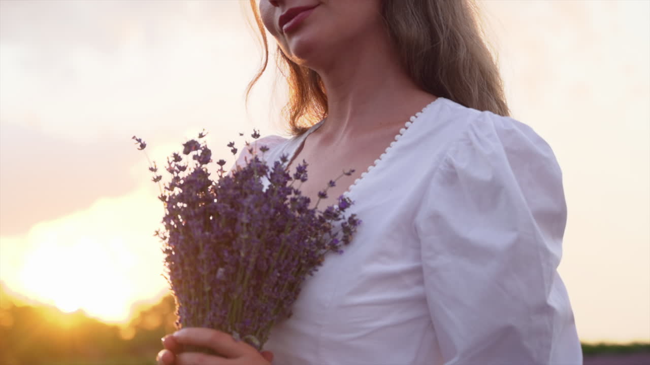 Woman in a white dress holding a bouquet of lavender in a field at sunset