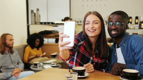 blanke vrouw en afro-amerikaanse man maken een selfie met smartphone in een café