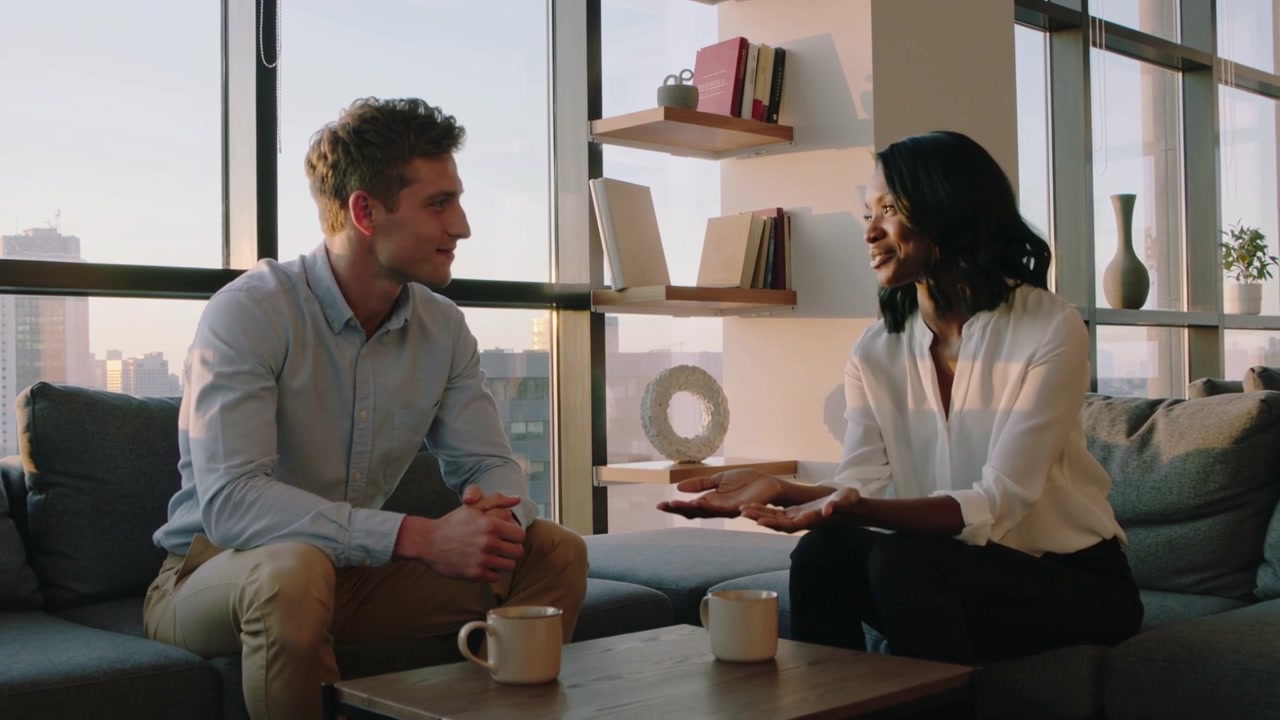 Starting business woman gesturing while man listening in highrise, mugs, skyline, building rapport