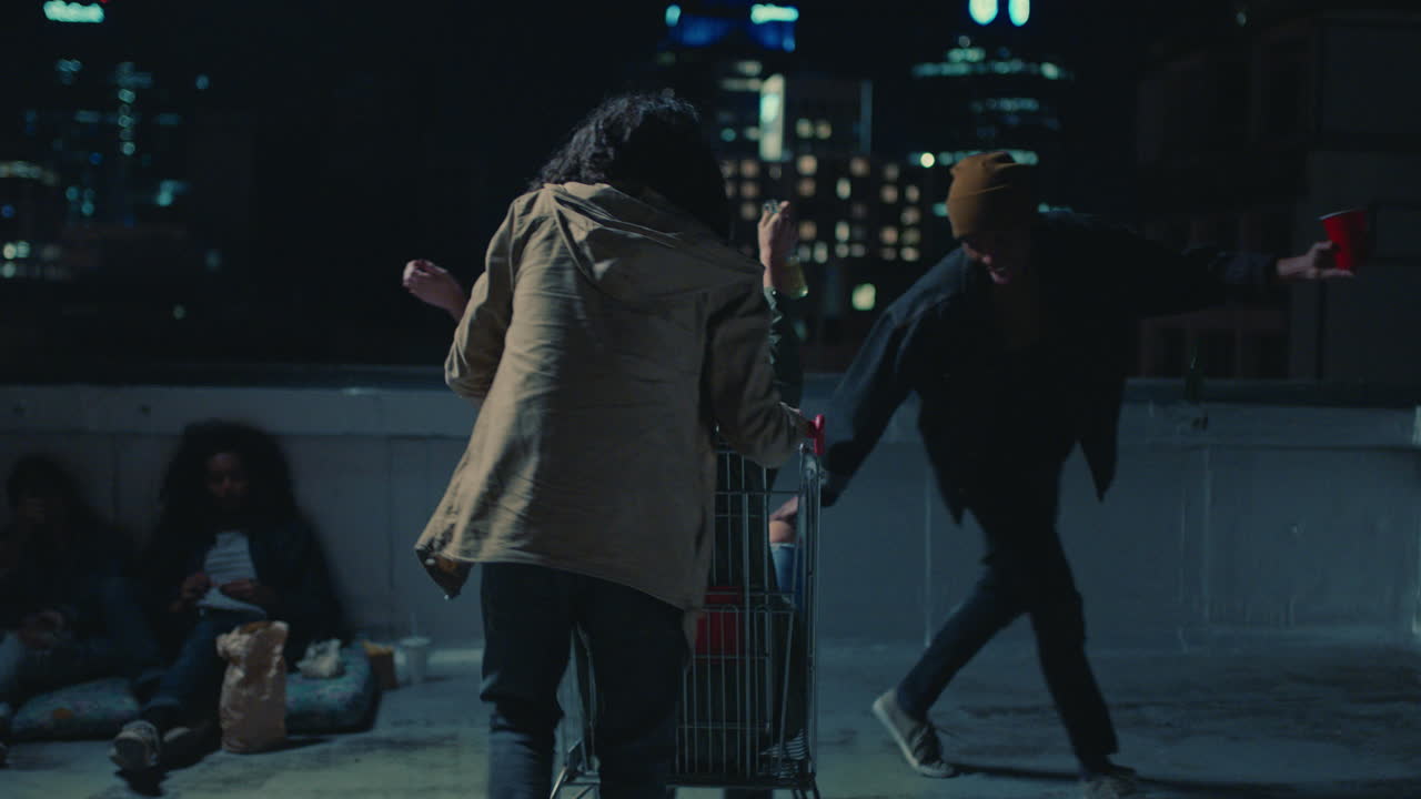 счастливая группа друзей играет с тележкой для покупок, веселится на крыше ночью, наслаждается вечеринкой на выходных.