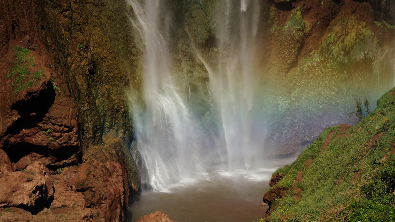 Sunlight creates a vibrant rainbow across cascading water at the base of Ouzoud Waterfalls in Morocco.