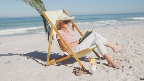 una mujer caucásica anciana sentada en las camas de sol en la playa.