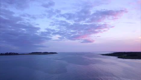 aerial shot flying out over a calm atlantic ocean harbor during a colorful soft pink and purple sunset off of kettle cove beach, maine.