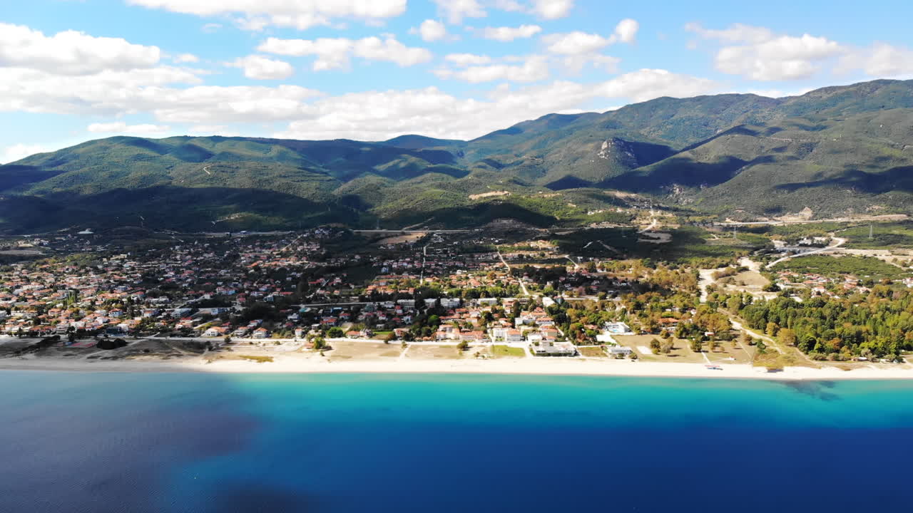 Asprovalta with multiple buildings and greenery, green hills on the background. Aegean sea coast. Long beach along the town. Sunny day. Greece