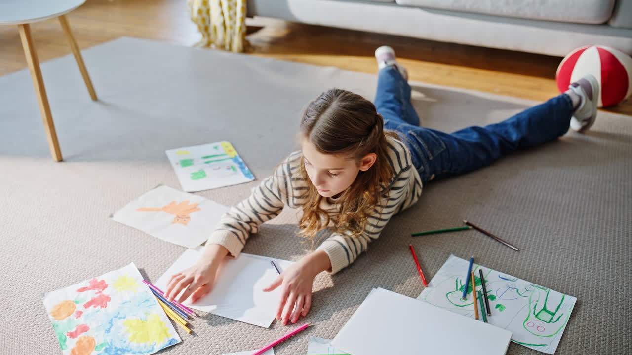 Talented child sketching lying home floor. Relaxed girl enjoying creative hobby