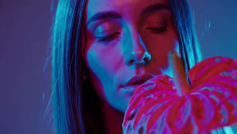 woman smelling a pink anthurium flower under vibrant neon lighting